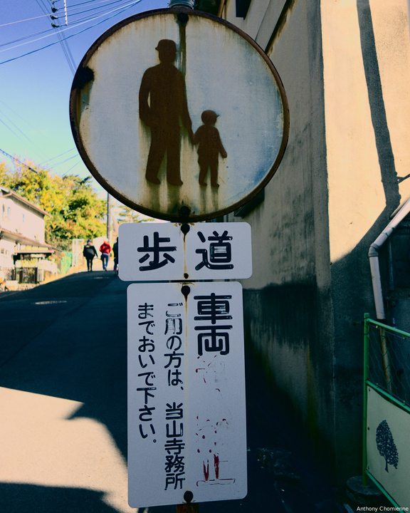 Un panneau de signalisation japonais rouillé avec un adulte tenant la main d'un enfant