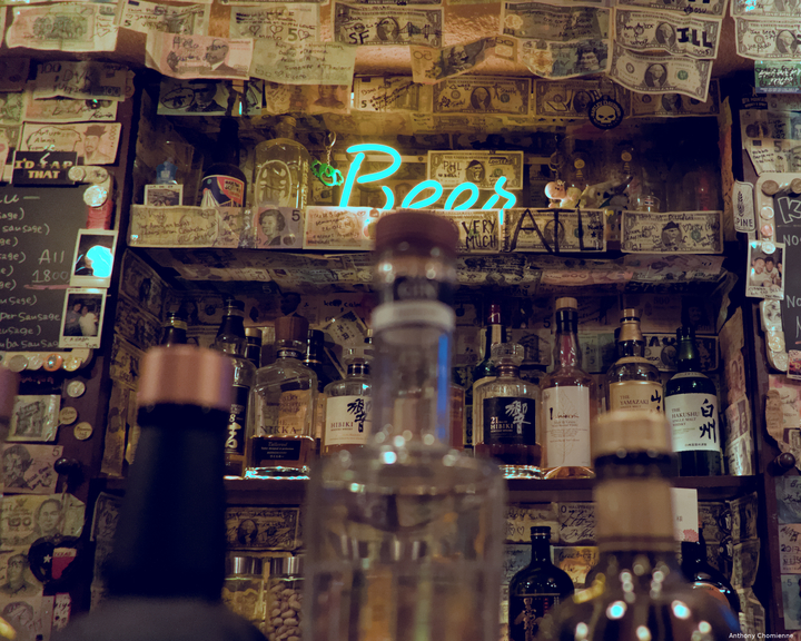 Le mur d'un bar avec plein de billet de banque de différent pays au mur avec au premier plan trois bouteilles flou